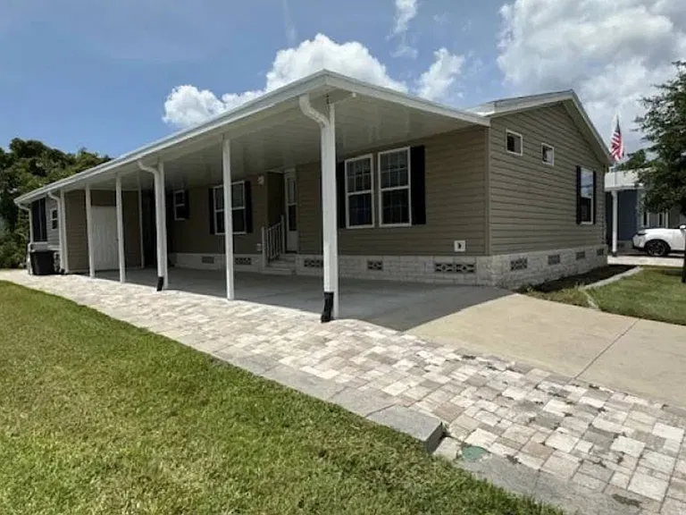 Tan 2019 manufactured home with a long covered carport and paver driveway in Walden Woods South, Homosassa